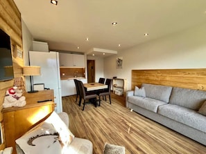 A modern living room with a sofa, dining table, and chairs. There is a kitchen area in the background. - 3rd floor, balcony, tv, ski locker, 38m², Les 2 Alpes (Mont-de-Lans)