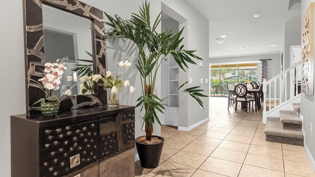 Ein modernes Interieur mit einem dunklen Holzschrank, einem großen Spiegel, weißen Orchideen, einer Topfpflanze, einer Essecke mit Tisch und Stühlen sowie einer Treppe.