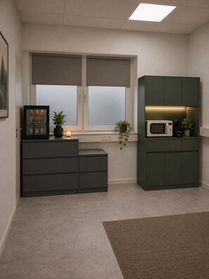 A modern kitchen with a built-in microwave, a cabinet, a window with blinds, a small plant, and a framed picture on a cabinet.