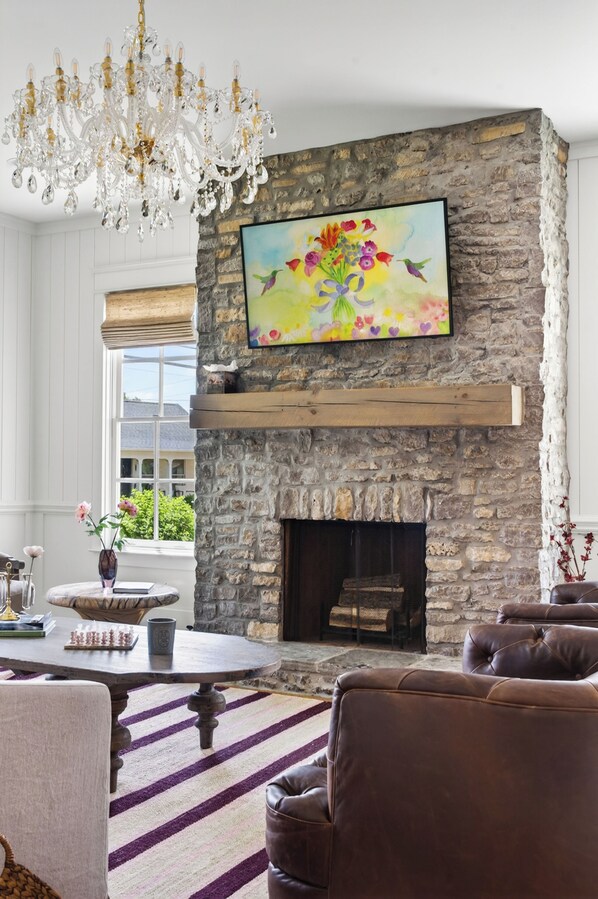 A stone fireplace with a mounted painting, a chandelier, and a view through a window.