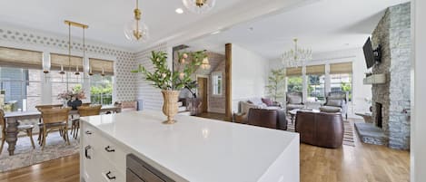 Een ruime keuken met een groot eiland, houten vloeren en hanglampen.