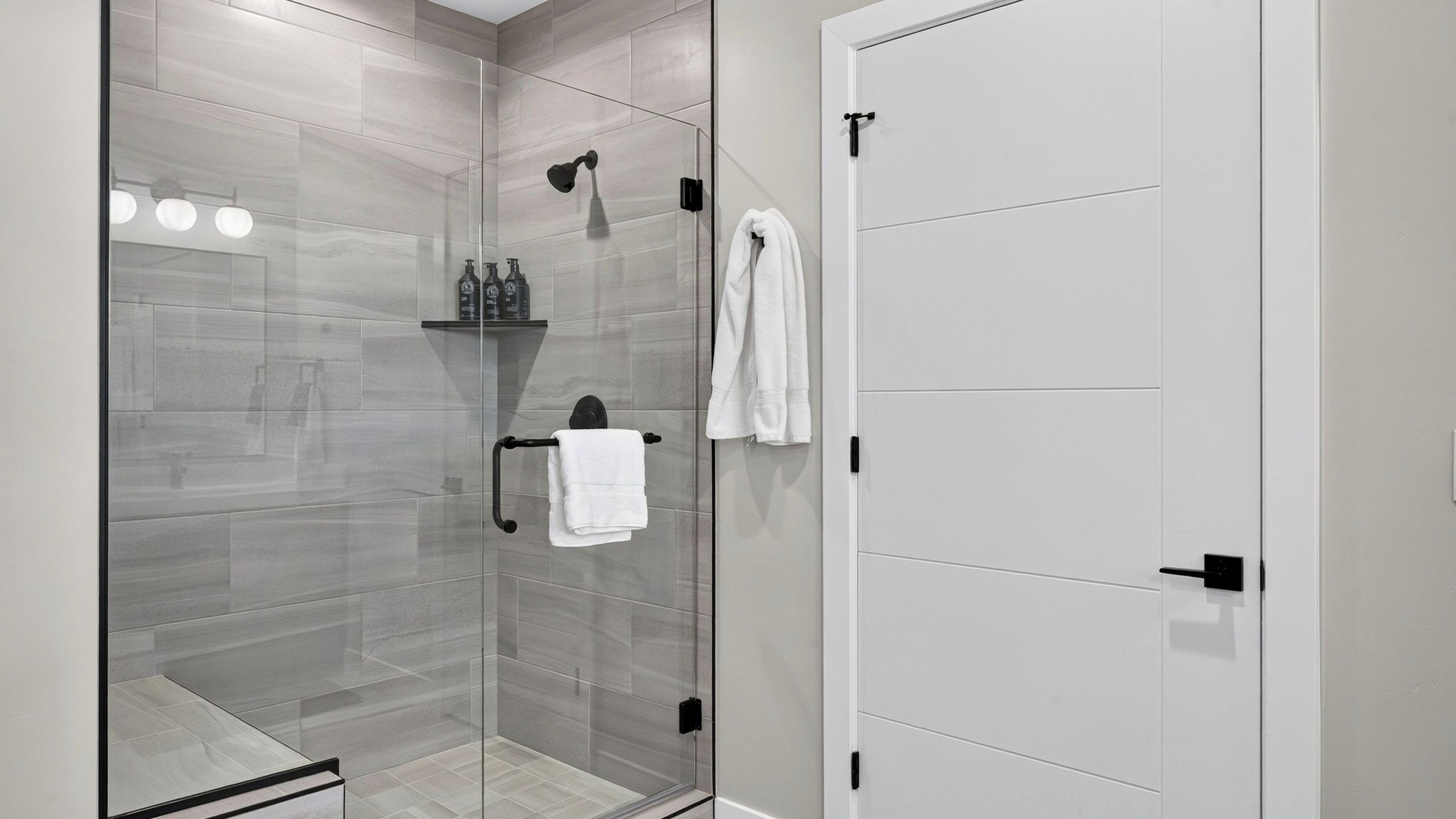 A modern bathroom with a glass-enclosed shower, a white door, and a towel rack.
