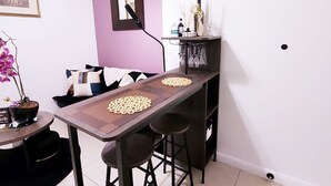A dining area with a long table, two bar stools, a small side table with a potted plant, and a wall-mounted mirror. - Cozy and comfy Apt. in the heart of Miami - 1-bedroom/1-bathroom with AC (Coral Gables)