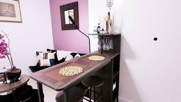 Un comedor con una mesa larga, dos taburetes de bar, una mesita auxiliar con una planta en maceta y un espejo montado en la pared.