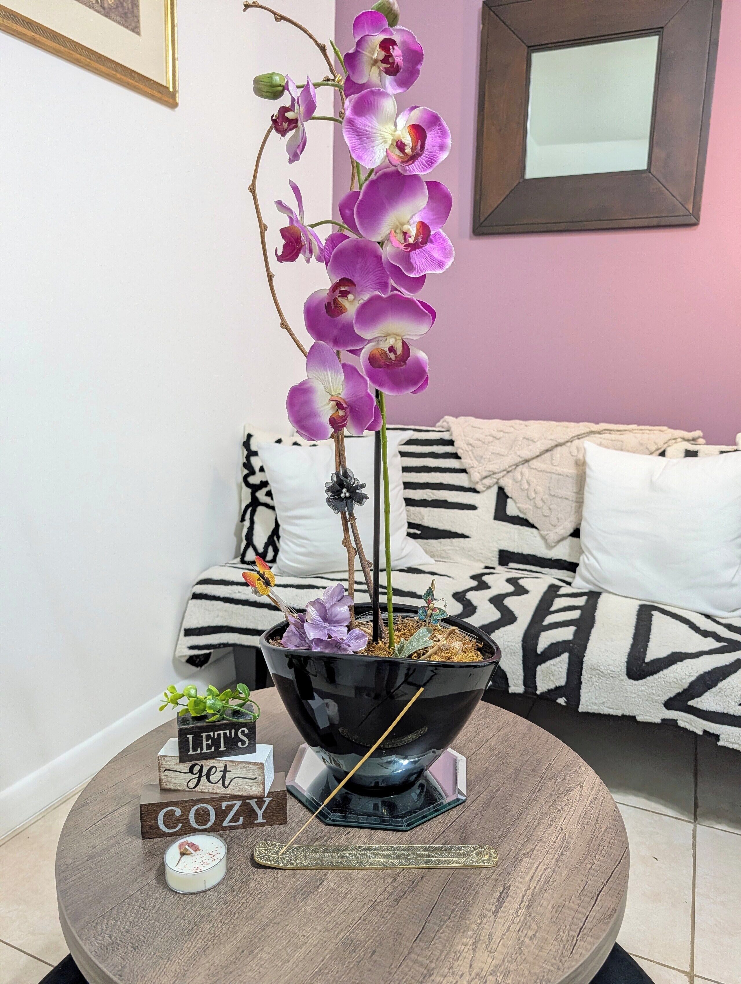A potted orchid on a round table with a sign that reads 'LET'S get COZY'.