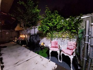 Ein Terrassenbereich im Freien mit einem weißen Stuhl und Tisch, umgeben von einem Holzzaun und Grünpflanzen.