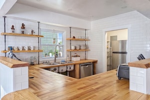 A modern kitchen with white tiled walls, wooden countertops, and built-in shelves.