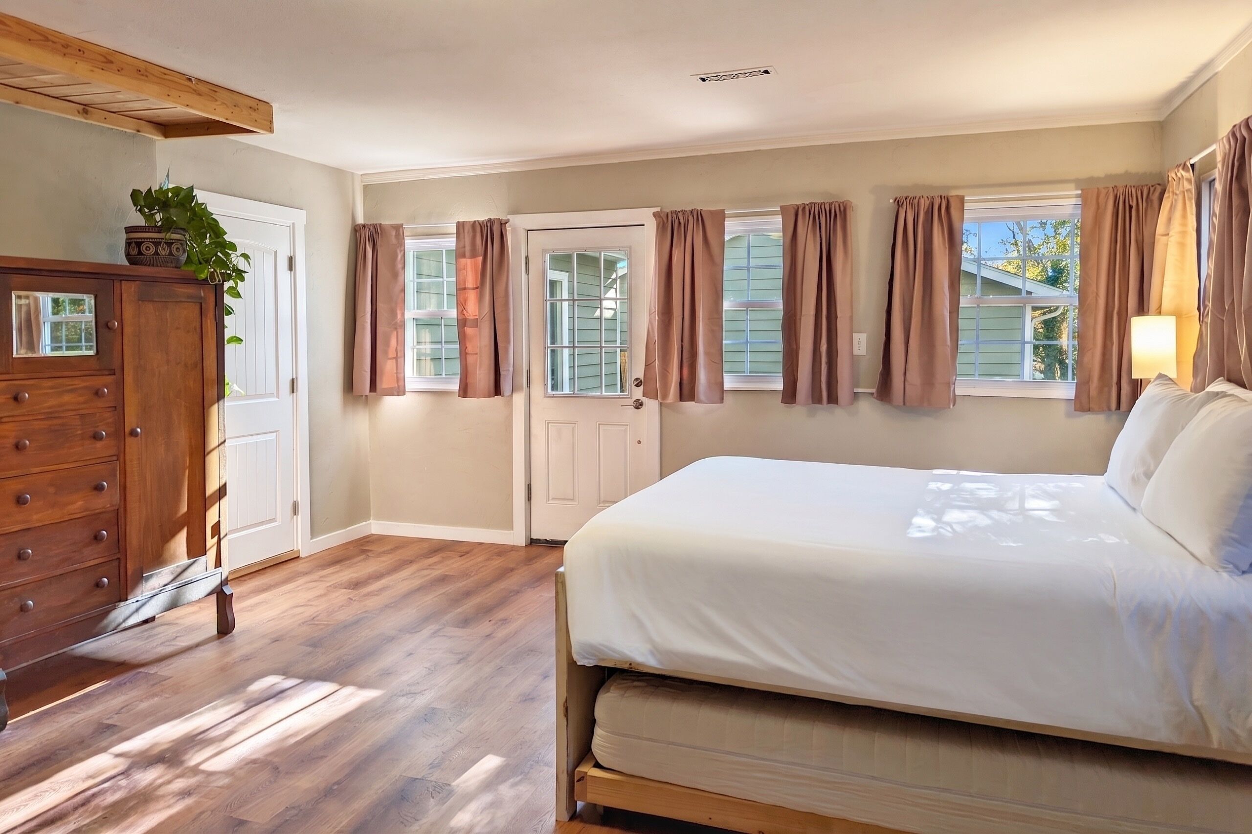 Un dormitorio con cama, cómoda de madera y puerta con cortinas.