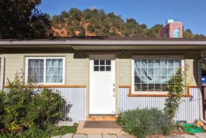 Una casa de un piso con puerta blanca, dos ventanas con cortinas, un porche pequeño y un jardín.