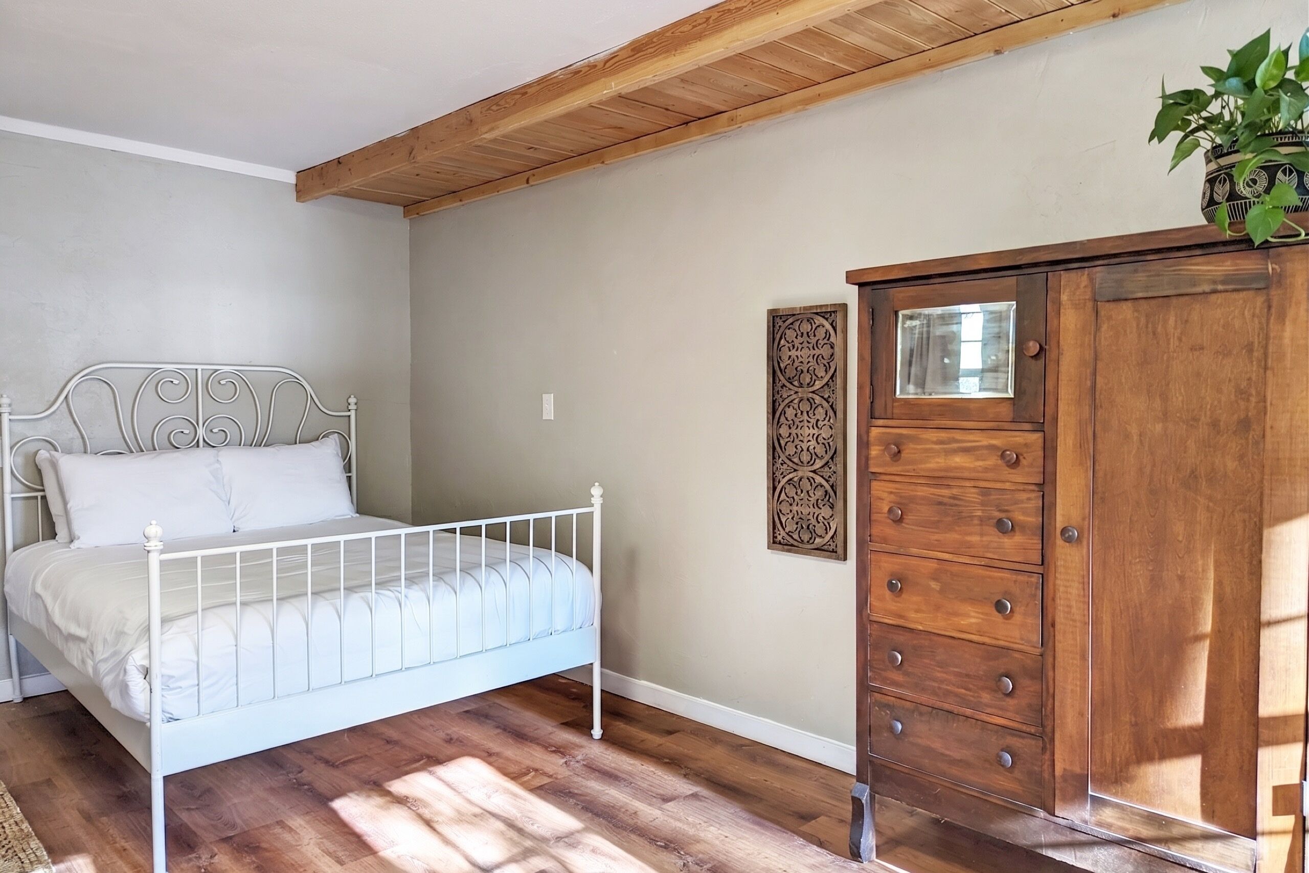 A bedroom with a metal bed frame, wooden dresser, and a decorative wall piece.