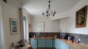 Una cucina con pavimento in legno, mobili color petrolio, un lampadario e un quadro appeso al muro.