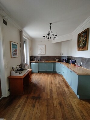A kitchen with wooden flooring, teal cabinetry, a chandelier, and a painting on the wall. - A charming, comfortable family home nestled between the sea and nature (Binic-Étables-sur-Mer)