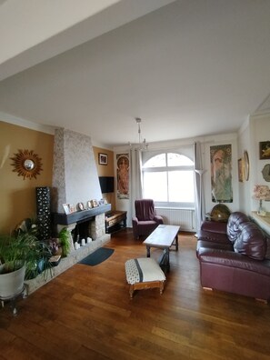 A living room with a fireplace, a sofa, a chair, and a table. - A charming, comfortable family home nestled between the sea and nature (Binic-Étables-sur-Mer)