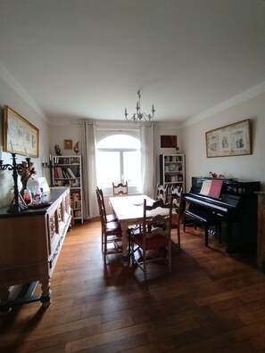 A dining area with a table, chairs, a piano, and bookshelves. - A charming, comfortable family home nestled between the sea and nature (Binic-Étables-sur-Mer)