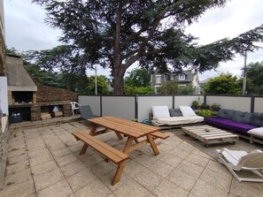 A patio with a wooden table and benches, a barbecue grill, and a seating area with cushions. - Vrbo Property (Binic-Étables-sur-Mer)