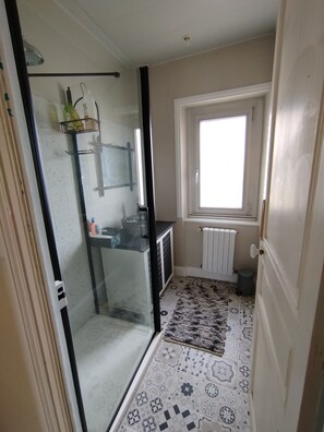 A bathroom with a glass shower enclosure, a sink with a mirror, a window, and a radiator. - Vrbo Property (Binic-Étables-sur-Mer)