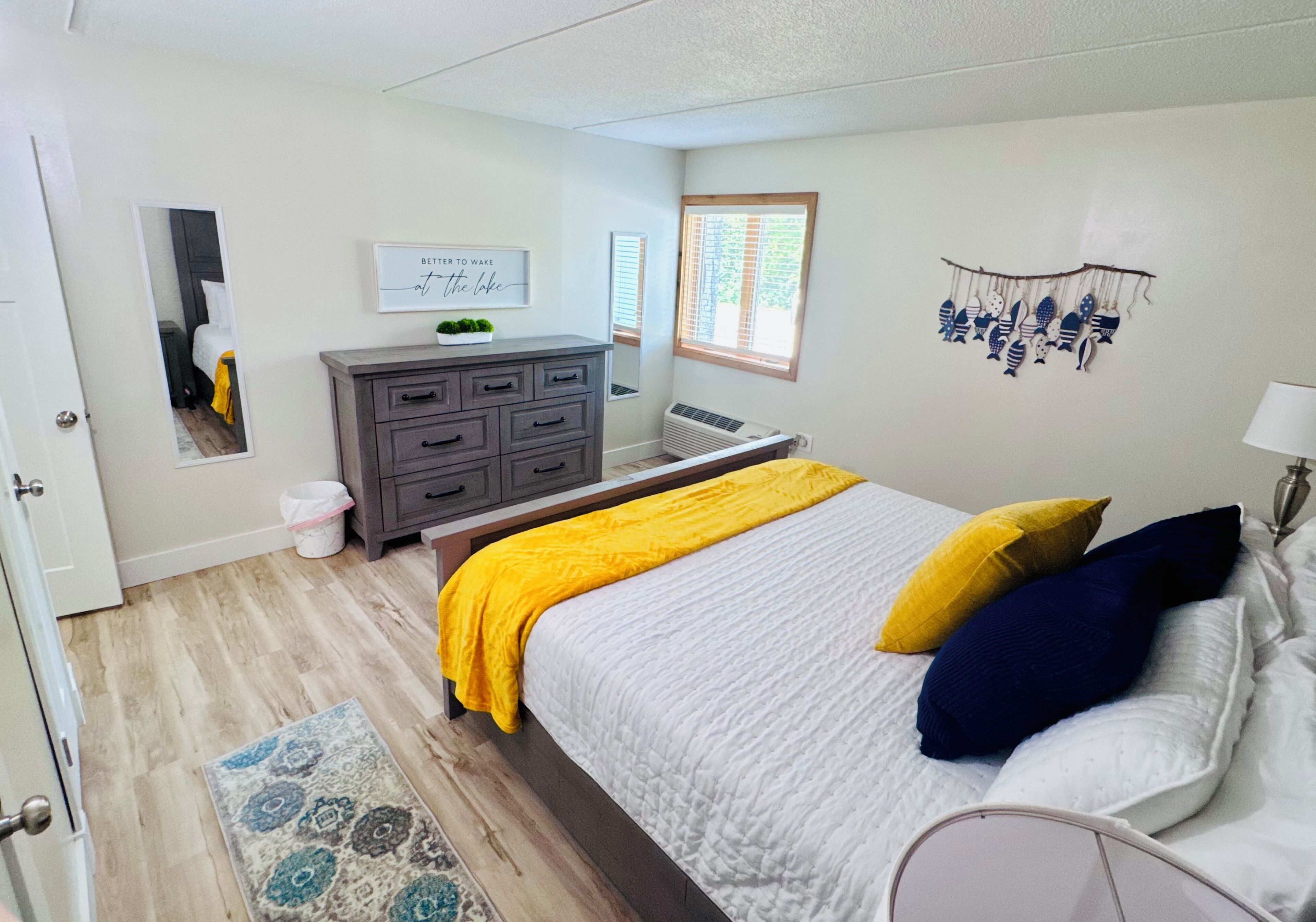 Een slaapkamer met een bed, een dressoir, een spiegel, een decoratie aan de muur en een raam.