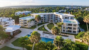 A modern hotel with a pool, surrounded by lush greenery and a clear view of the distant landscape. - The Surfin Turtle | Luxury Oceanfront Condo at the WAVE in Encuentro (Cabarete)
