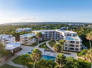 A modern hotel with a pool, surrounded by lush greenery and a clear view of the distant landscape. - The Surfin Turtle | Luxury Oceanfront Condo at the WAVE in Encuentro (Cabarete)