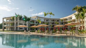 A hotel with a swimming pool, sun loungers, and palm trees. - The Surfin Turtle | Luxury Oceanfront Condo at the WAVE in Encuentro (Cabarete)