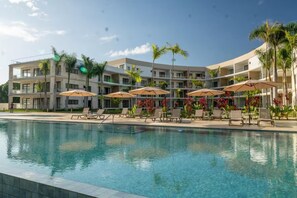 A hotel with a swimming pool, sun loungers, and palm trees. - The Surfin Turtle | Luxury Oceanfront Condo at the WAVE in Encuentro (Cabarete)