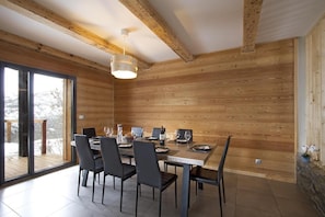 A dining area with a wooden interior, a large table set for four, and a view through a glass door. - Chalet, 40m from ski slopes, terrace, tv, 140m², Les 2 Alpes (Mont-de-Lans)