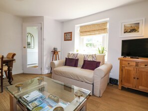 A living room with a sofa, a glass coffee table, a television, a wooden cabinet, and a window with a view of the outdoors. - Sunnyside (Matlock)