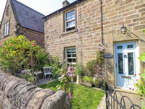 A stone cottage with a blue door, a garden with flowers, and a white chair. - Sunnyside (Matlock)