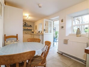 A dining area with a round table, chairs, a kitchen in the background, and a window with a view. - Sunnyside (Matlock)