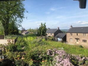 A rural setting with traditional stone houses, a garden with flowering plants, and a clear sky. - Sunnyside (Matlock)