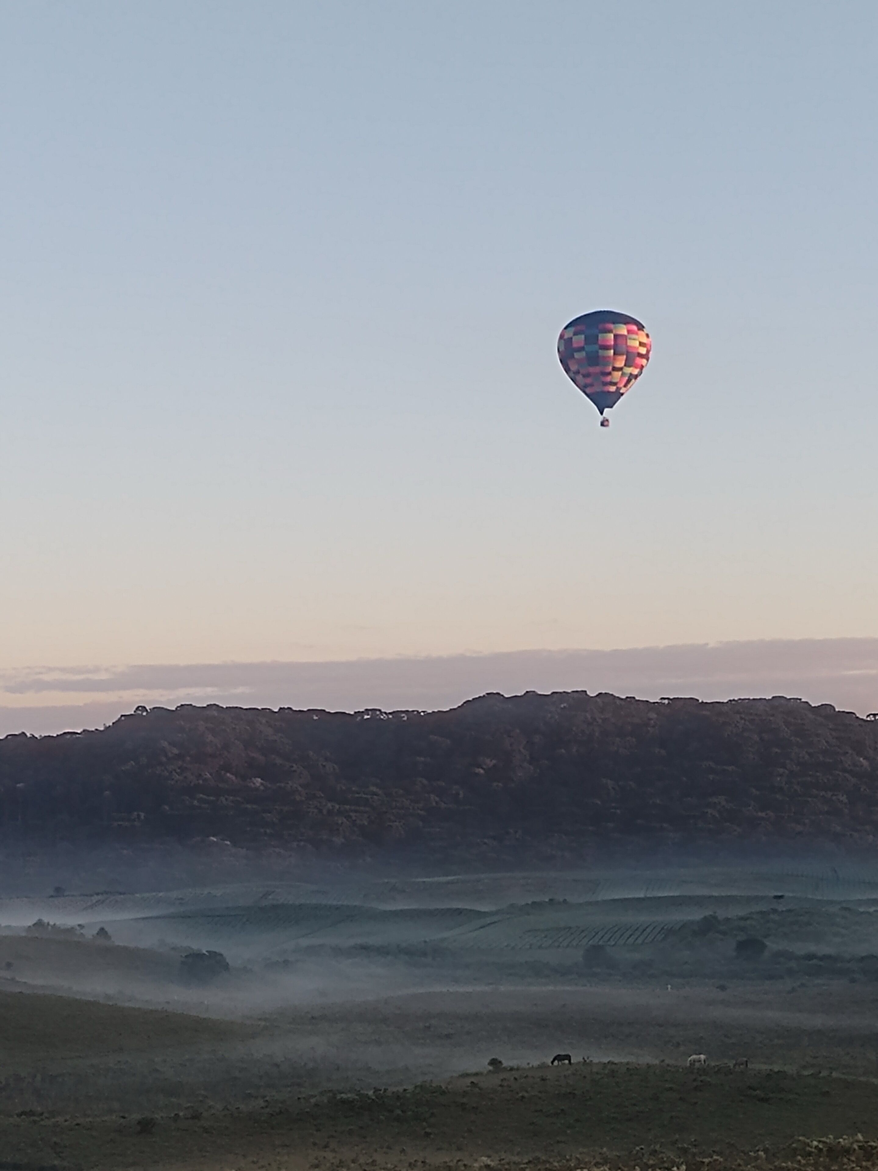 Un ballon à air chaud dans le ciel, au-dessus d’un paysage vallonné.