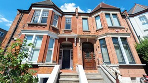 A Victorian-style brick house with a bay window, a front door, and a staircase leading to the entrance. - Cosy Little Flat - Perfect Base for Explorers (London)