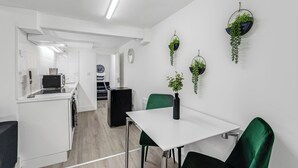 A modern kitchen with white cabinets, a black refrigerator, and a dining area with a white table and green chairs. - Cosy Little Flat - Perfect Base for Explorers (London)