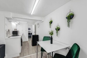 Eine moderne Küche mit weißen Schränken, einem schwarzen Kühlschrank und einem Essbereich mit weißem Tisch und grünen Stühlen.