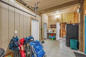 A garage with a door, a refrigerator, a broom, and various bags. - Crystal Beach Serenity Escape: 4BR Beachfront! Stunning Views & Outdoor Showers (Bolivar Peninsula)