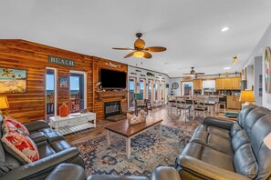 A spacious living room with a fireplace, leather sofas, and a wooden wall with a 'BEACH' sign. - Crystal Beach Serenity Escape: 4BR Beachfront! Stunning Views & Outdoor Showers (Bolivar Peninsula)