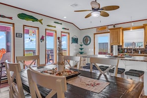 Un interior decorado con motivos costeros, con comedor, cocina y grandes ventanales con vistas al mar.