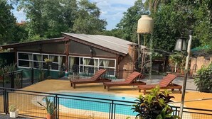 A pool area with lounge chairs, a building with large windows, and a water tank. - Lost & Found Iguazú Hostel (Puerto Iguazu)