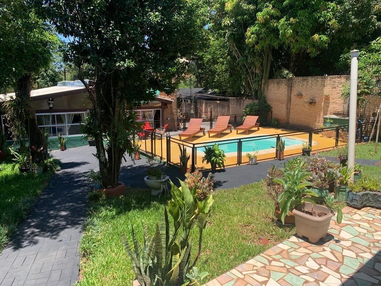 A pool area with lounge chairs, a brick wall, and potted plants.