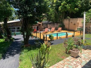 A pool area with lounge chairs, a brick wall, and potted plants.