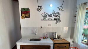 A kitchen with a sink, countertop, wooden cabinet, and a small table with a kettle and cup. - Lost & Found Iguazú Hostel (Puerto Iguazu)