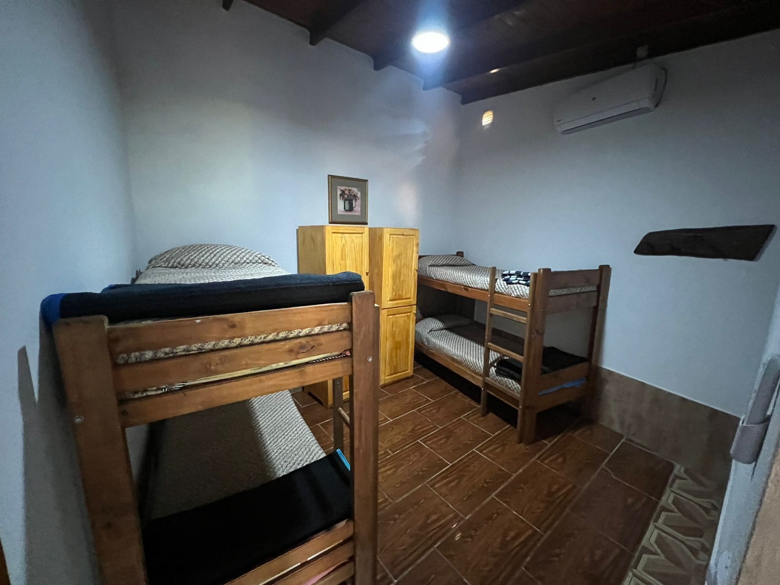 Una habitación pequeña y funcional con literas, un armario de madera y un cuadro en la pared.