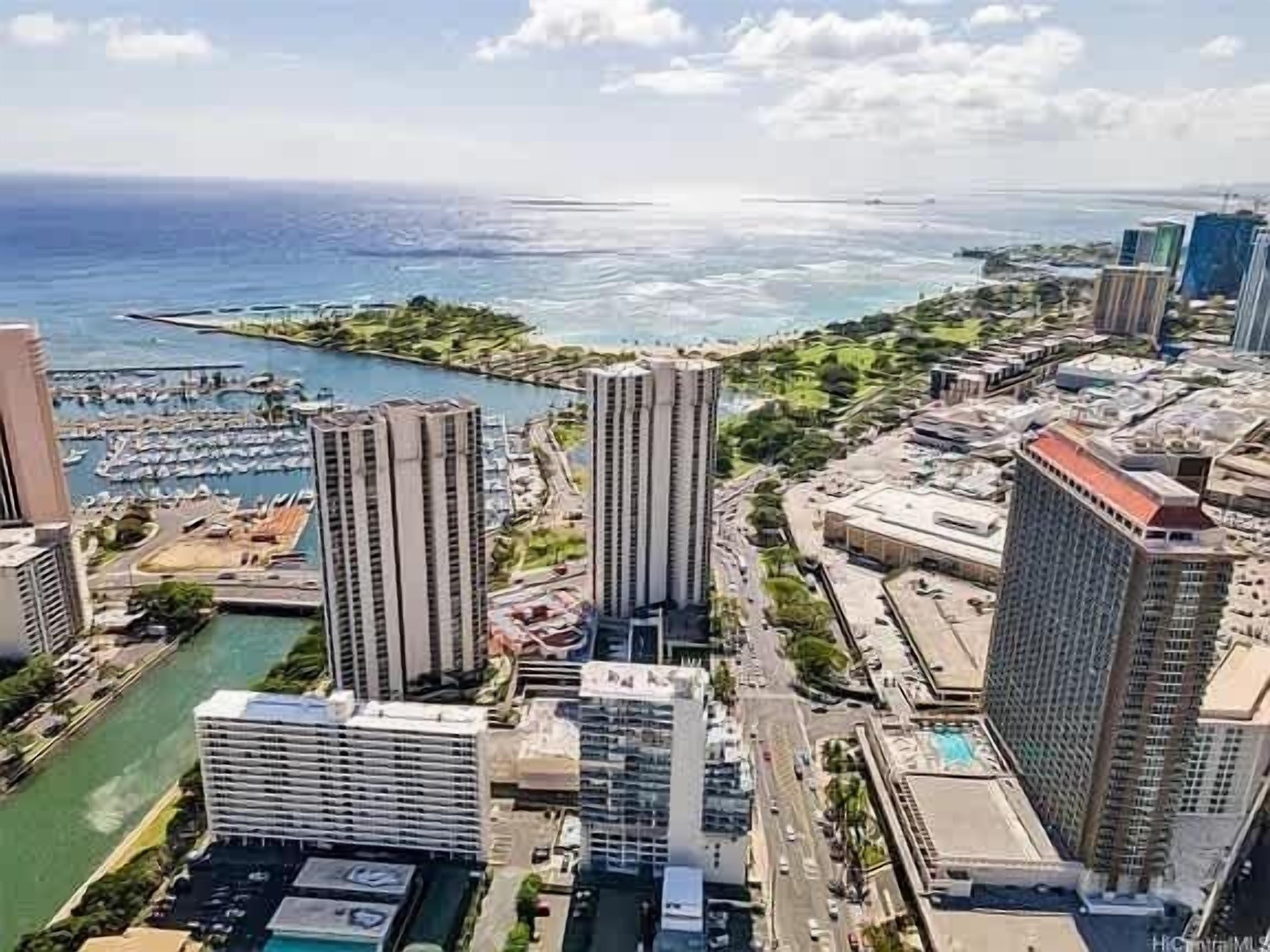 A high-rise hotel with multiple floors, a marina with boats, and a view of the ocean.