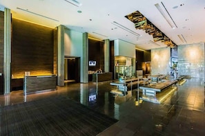 Eine moderne Lobby mit Empfangsschalter, Sitzgelegenheiten und einem großen Spiegel, der den Raum widerspiegelt.