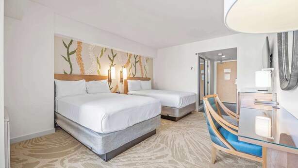 Ein Hotelzimmer mit zwei Betten, einem Schreibtisch, einem Stuhl und einem großen Spiegel.