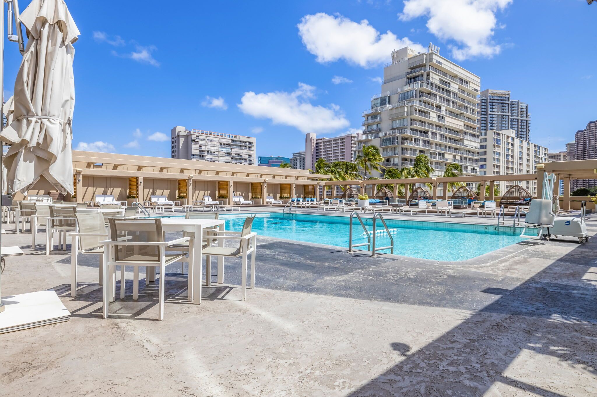 Area piscina di un hotel con lettini e ombrelloni, circondata da edifici alti.