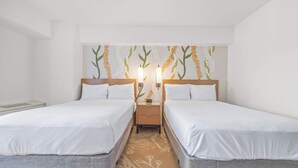 Ett hotellrum med två separata sängar, ett nattduksbord med en lampa och en vägg med ett blommönster.
