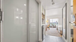 En hotellkorridor med modern design, som leder till ett sovrum med balkong och utsikt över staden.