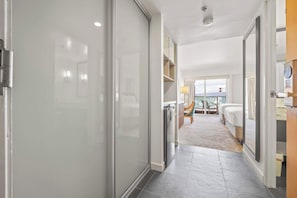 Een hotelgang met een modern design, die leidt naar een slaapkamer met een balkon en uitzicht op de stad.