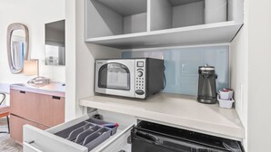 Eine kleine Küche mit integriertem Mikrowellenherd, einer Kaffeemaschine und einem schwarzen Kühlschrank.